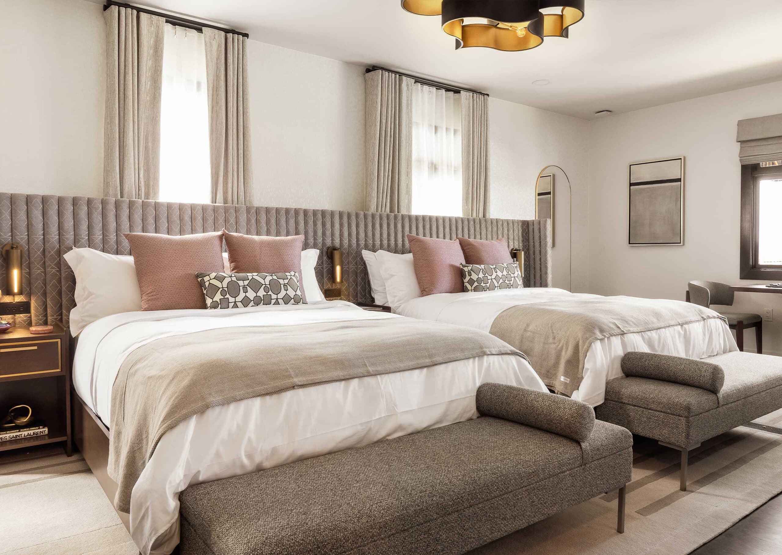 Luxury hotel room with two queen beds, upholstered headboards, layered neutral bedding, and elegant bedside lighting