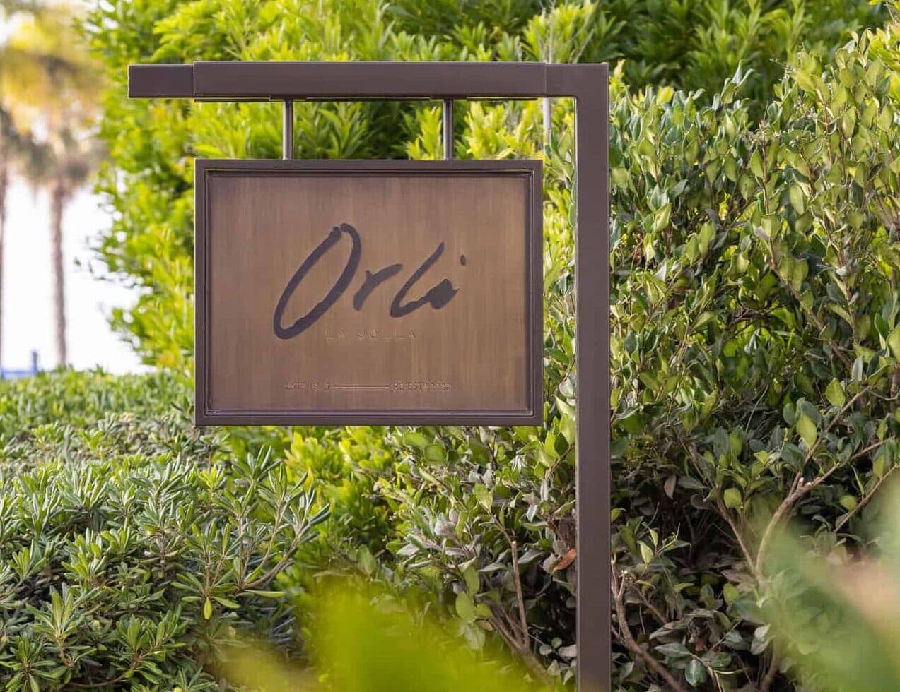 Outdoor wooden sign displaying the Orli name, surrounded by lush greenery.