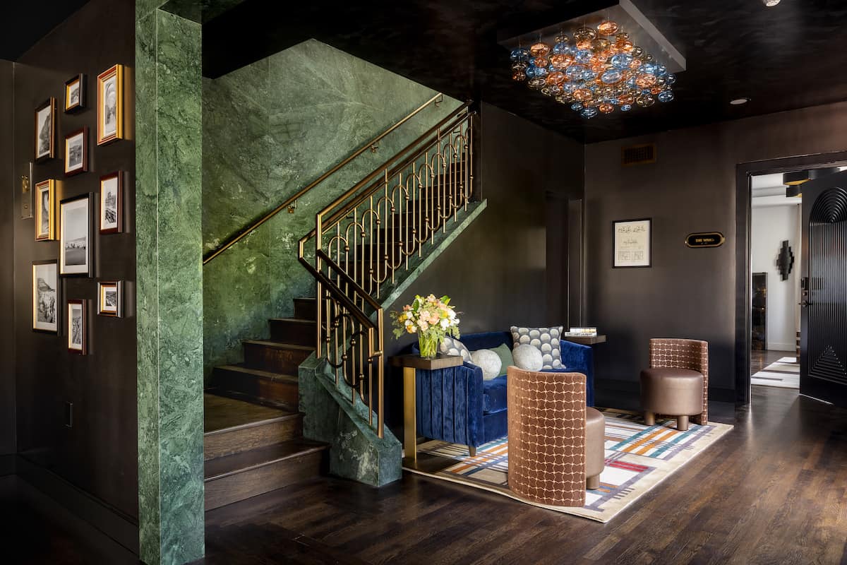 Stylish modern interior featuring a staircase, dark walls, contemporary seating, and a decorative chandelier.