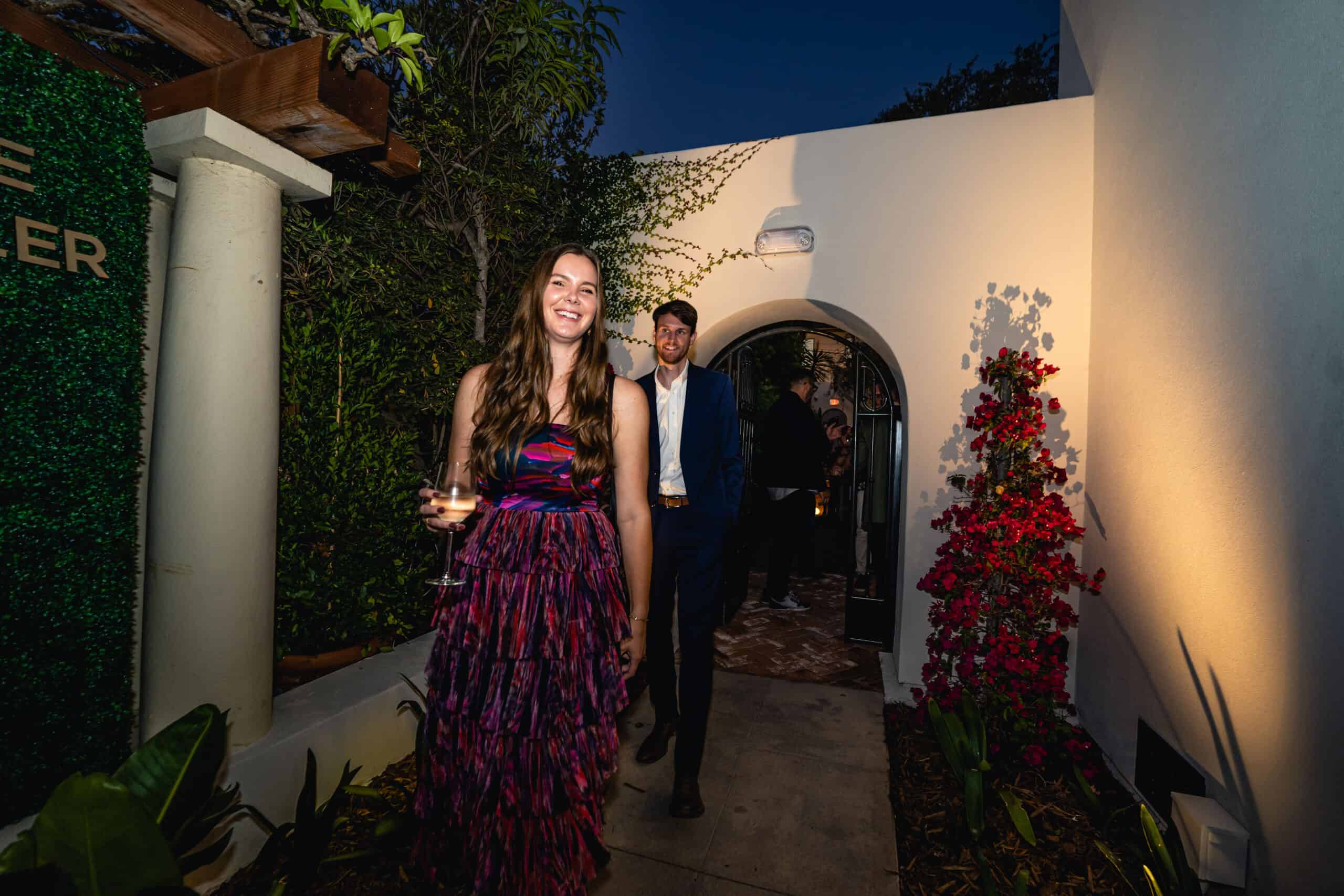 Guests arriving at an evening event through an arched courtyard entrance, dressed in elegant attire.