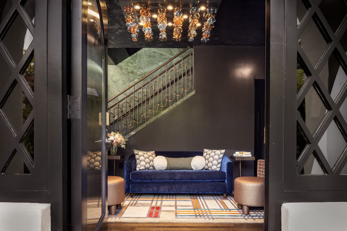 Elegant hotel entryway featuring a blue velvet sofa, decorative pillows, and a staircase with patterned tile backdrop