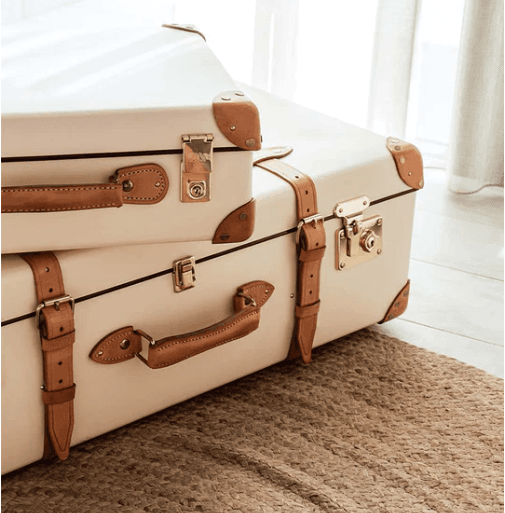 Stacked cream-colored vintage suitcases with leather straps placed on a woven rug in a bright interior