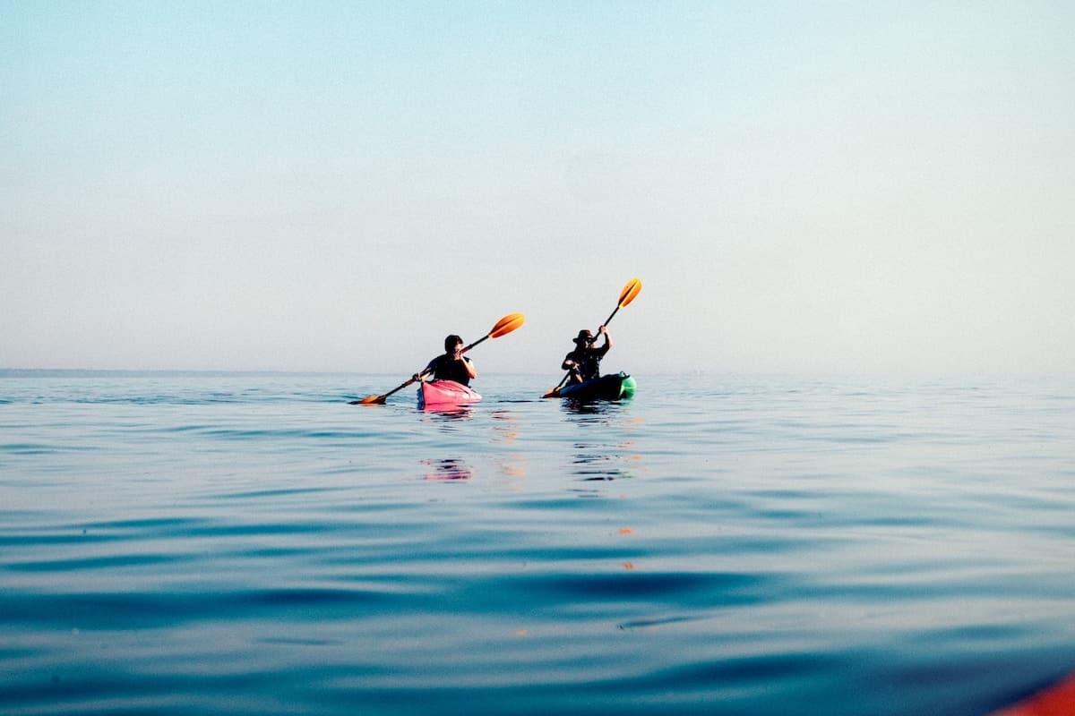 Two people kayaking on calm open ocean water under a clear sky, paddling toward the horizon in colorful kayaks.”