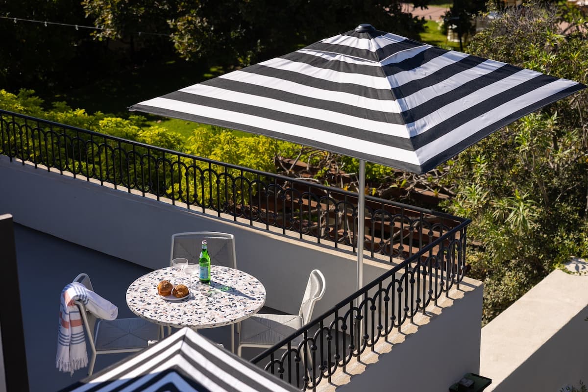 Private outdoor patio with striped umbrella, wrought iron table, and chairs overlooking lush greenery in a boutique hotel setting