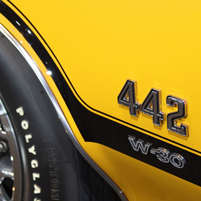 Close-up of a yellow classic car panel featuring “442 W-30” badge and black racing stripe near the rear wheel
