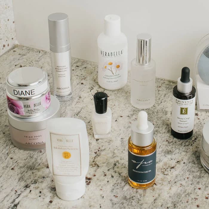 Assorted luxury skincare products including serums, creams, and facial oils arranged on a marble bathroom countertop