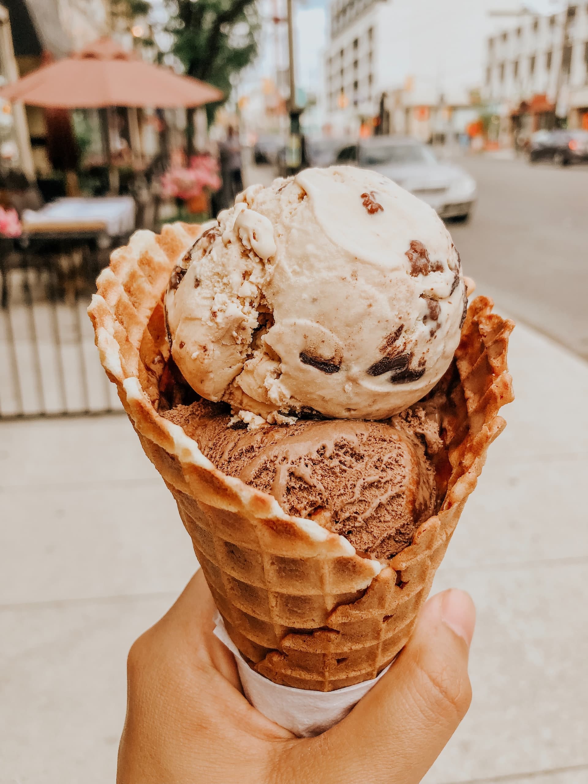 person holding an ice cream in a waffle cone. there is a cityscape behind the ice cream cone.