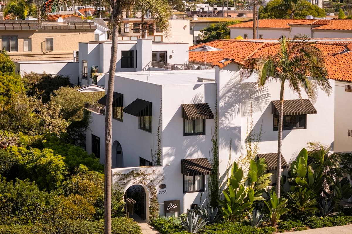 White Mediterranean-style building with terracotta roof tiles, palm trees, and lush greenery in a sunlit coastal setting