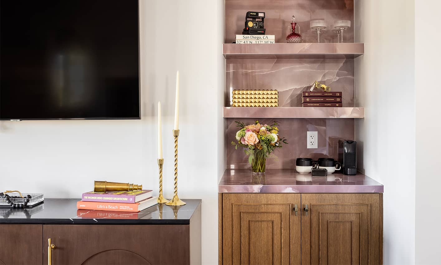 Built-in shelving with marble surfaces, decorative books, flowers, and coffee station beside a wall-mounted TV.