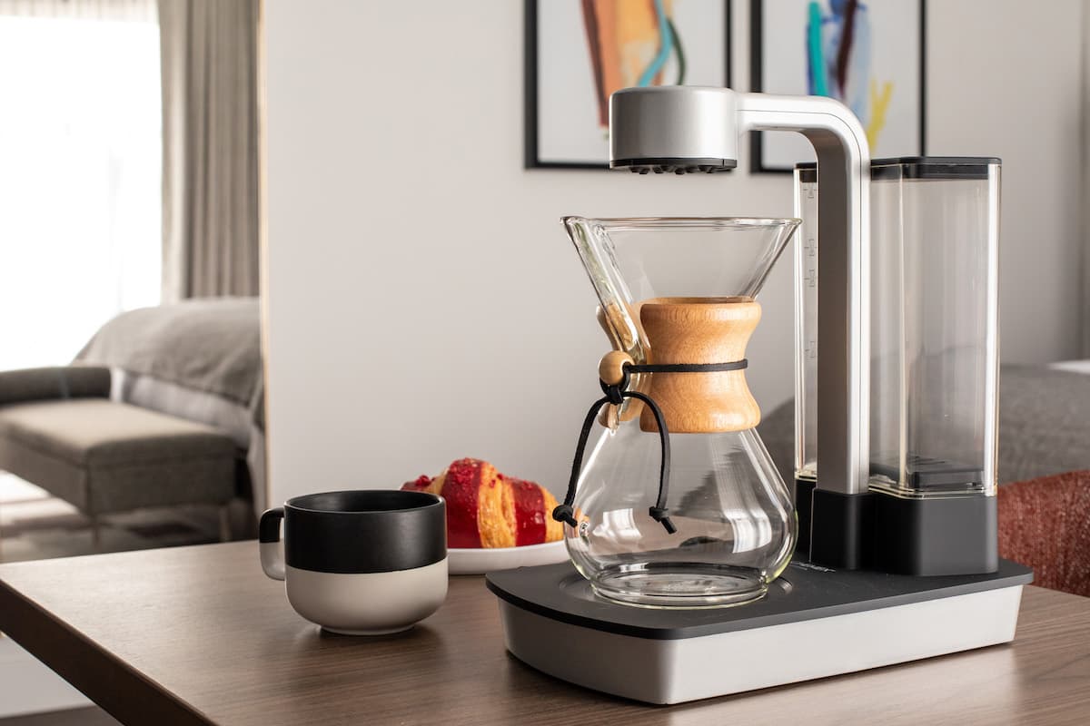 Modern pour-over coffee maker set on a wooden table with a cup, framed artwork, and soft natural light in a stylish interior