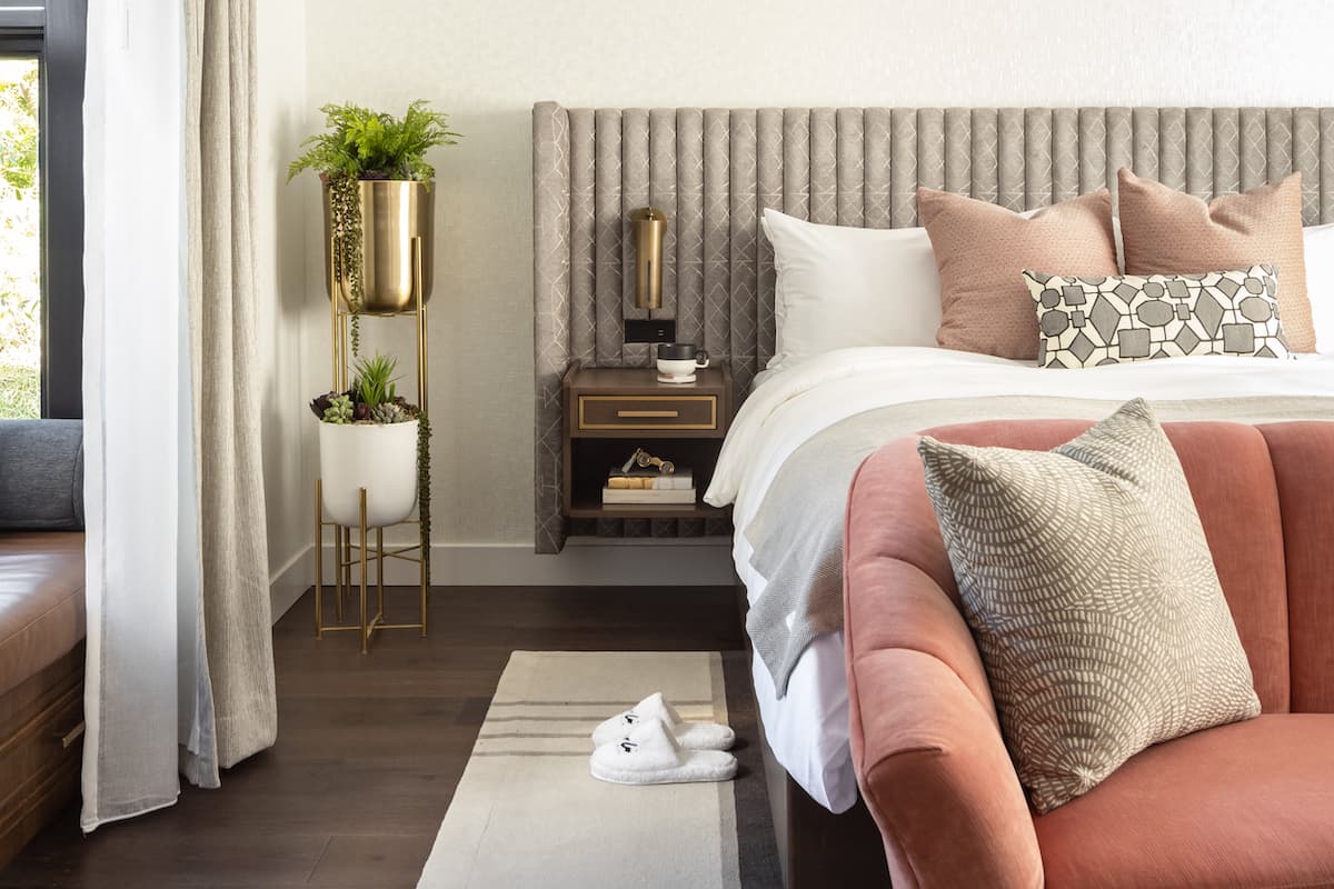 Luxury hotel bedroom detail with upholstered bed, blush accent sofa, bedside table, and layered neutral décor