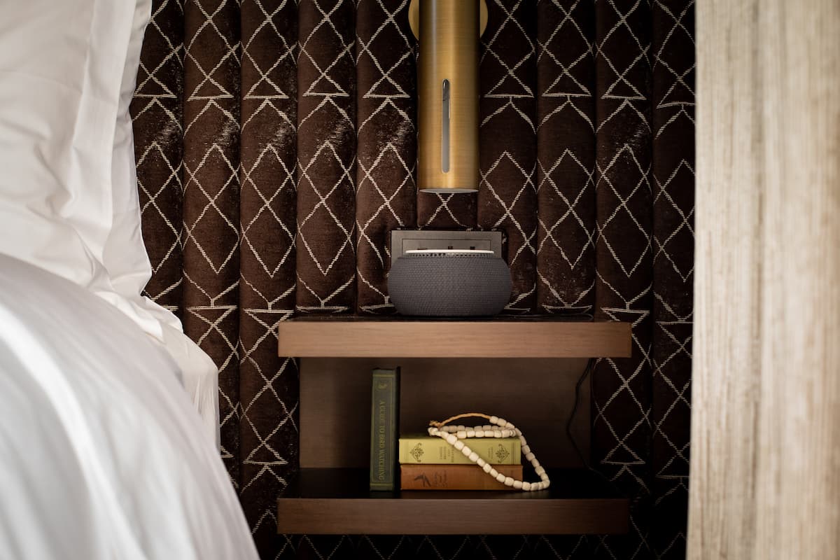 Hotel bedside shelf with modern lamp, decorative books, and textured upholstered wall paneling in a luxury bedroom setting