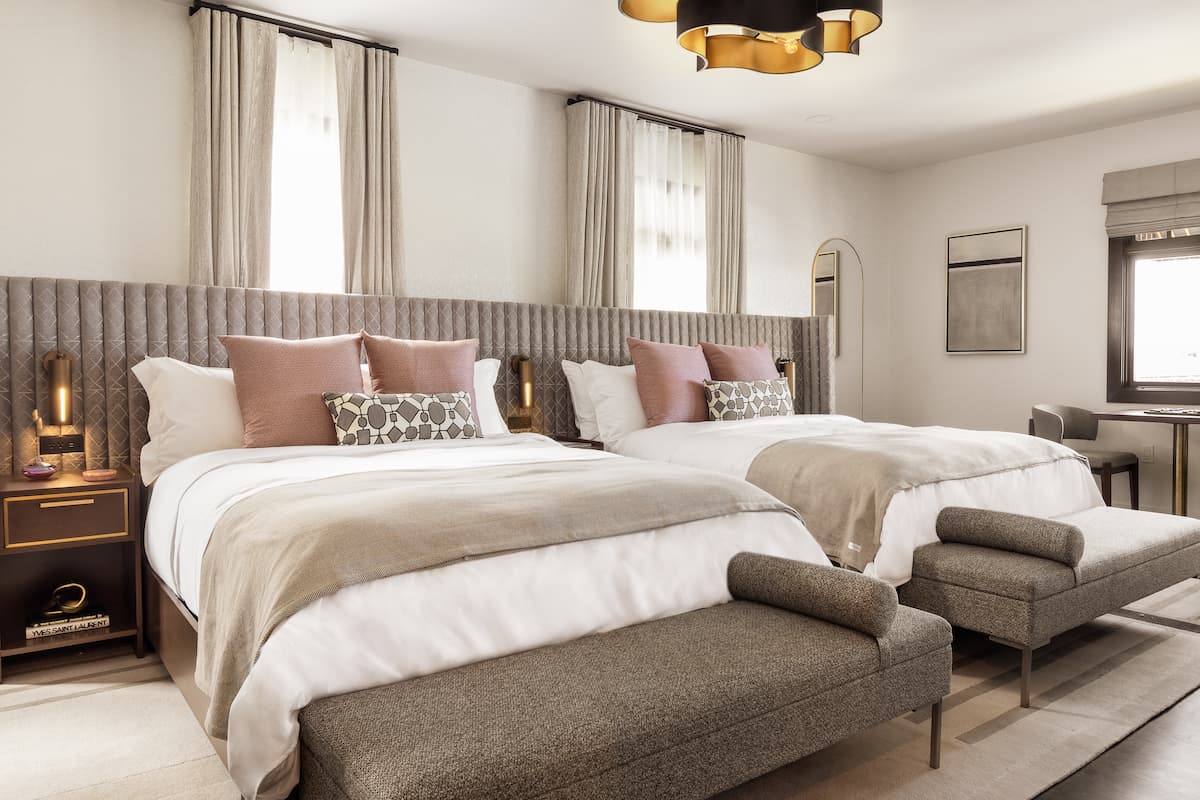 Luxury hotel room with two queen beds, upholstered headboards, layered neutral bedding, and soft natural light