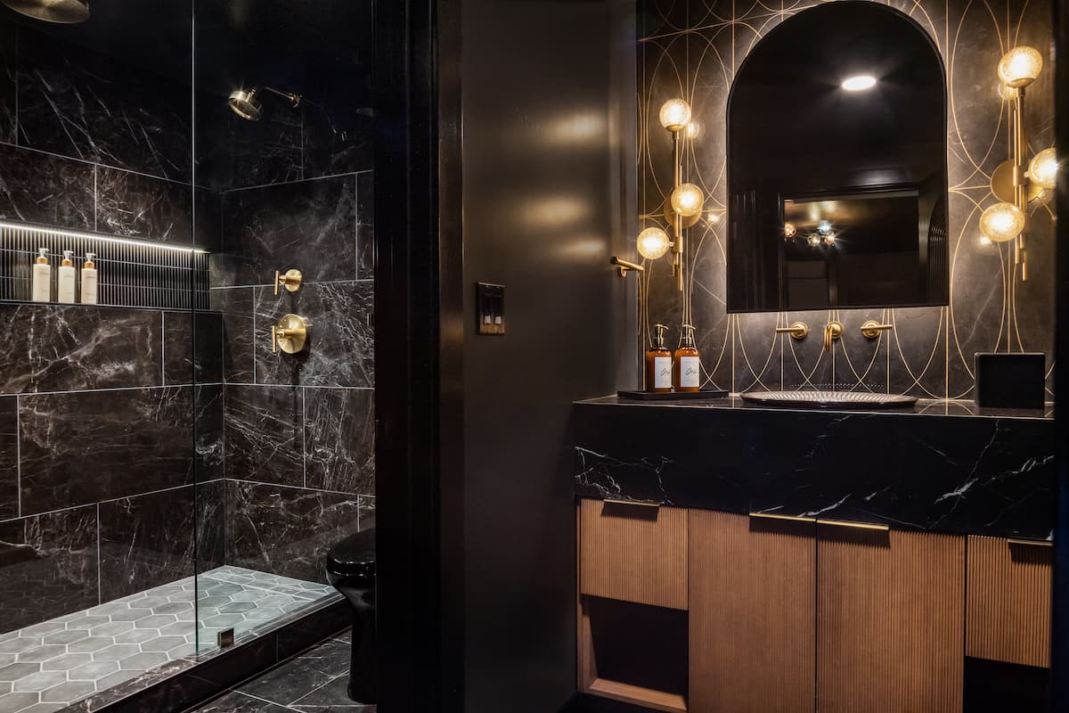 Luxury bathroom with black marble walls, modern vanity, and gold accent lighting in an upscale hotel interior