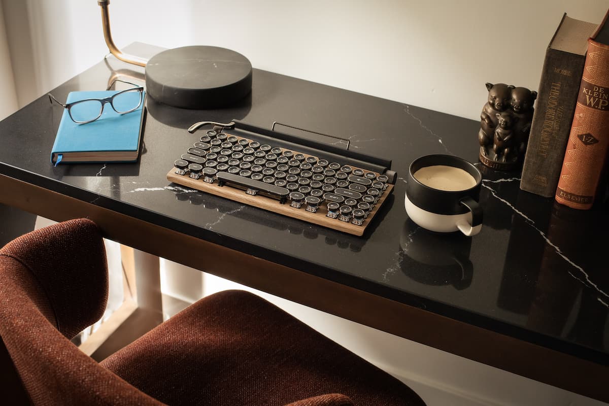 Modern writing desk with a keyboard, coffee cup, books, and reading glasses in a stylish, softly lit home or hotel workspace