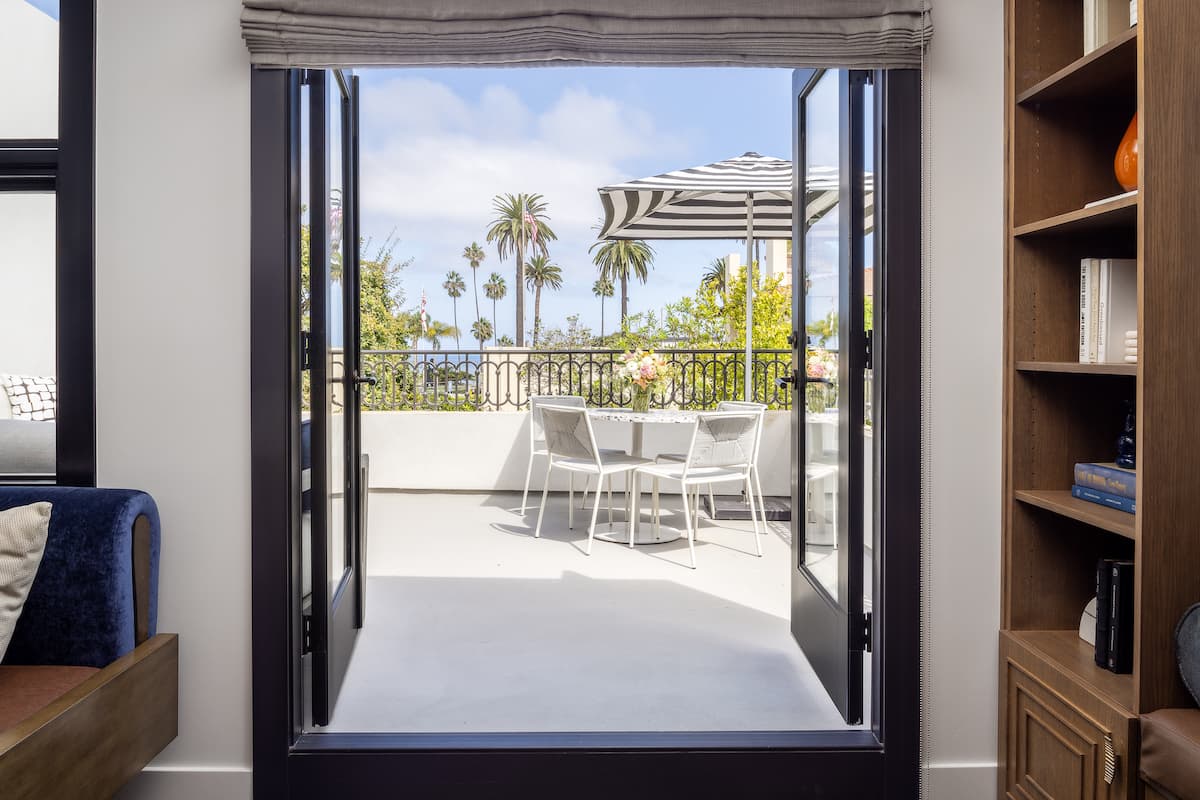 Open French doors leading to a private terrace with outdoor dining furniture and palm tree views in a luxury hotel suite