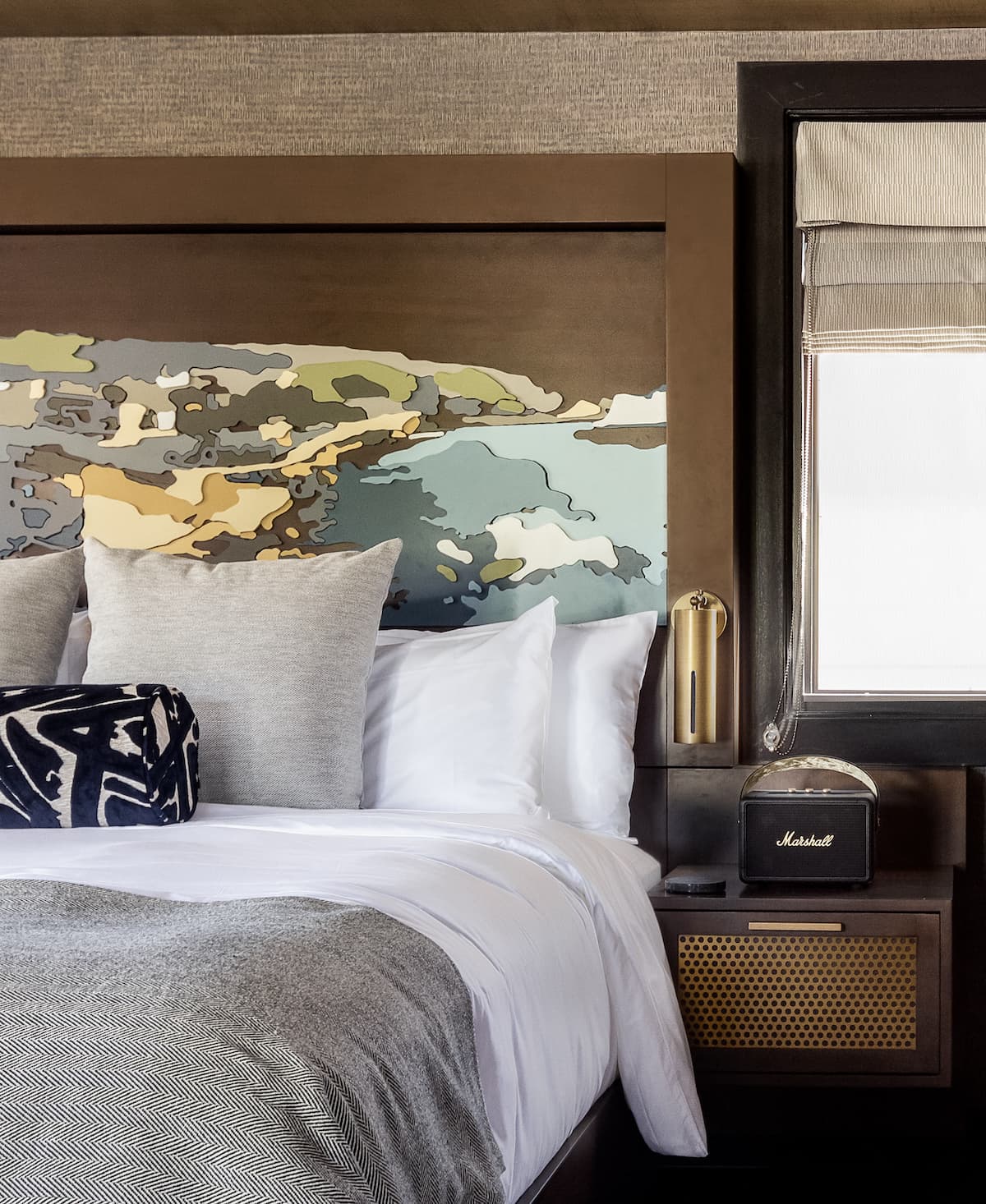 Luxury hotel bedroom with layered bedding, abstract headboard artwork, and modern bedside lighting in a refined interior design