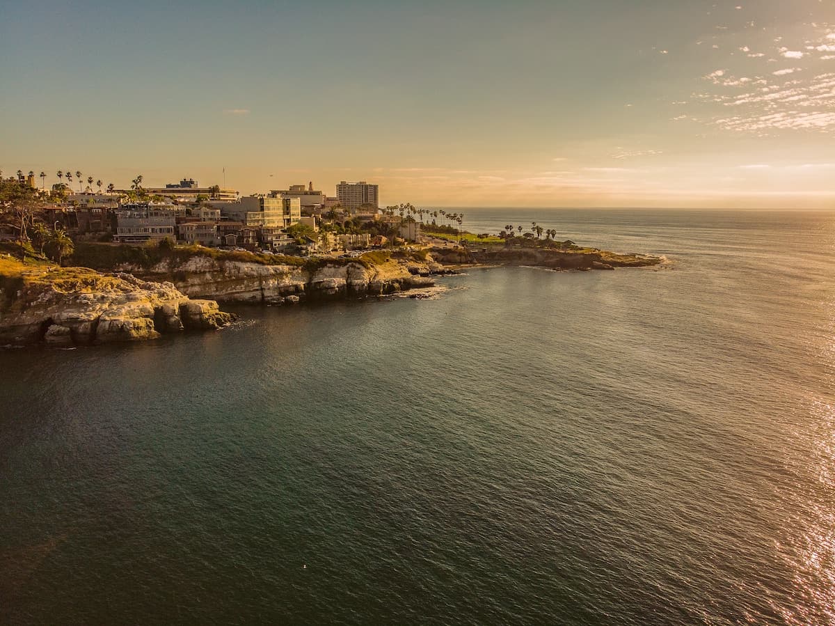 Coastal cityscape overlooking calm ocean waters and rocky shoreline during golden hour at sunset