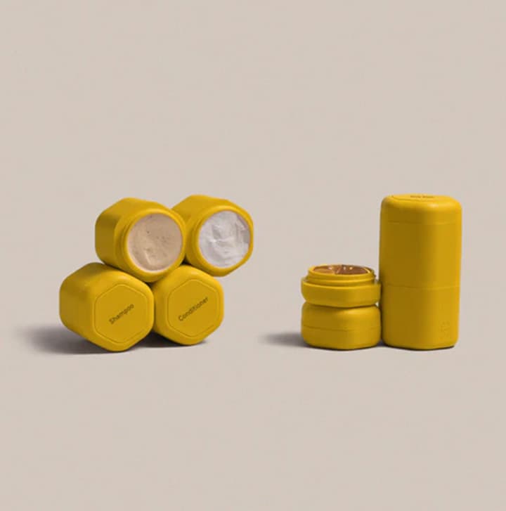 Stack of yellow reusable travel containers with open and closed lids displayed on a minimalist neutral background