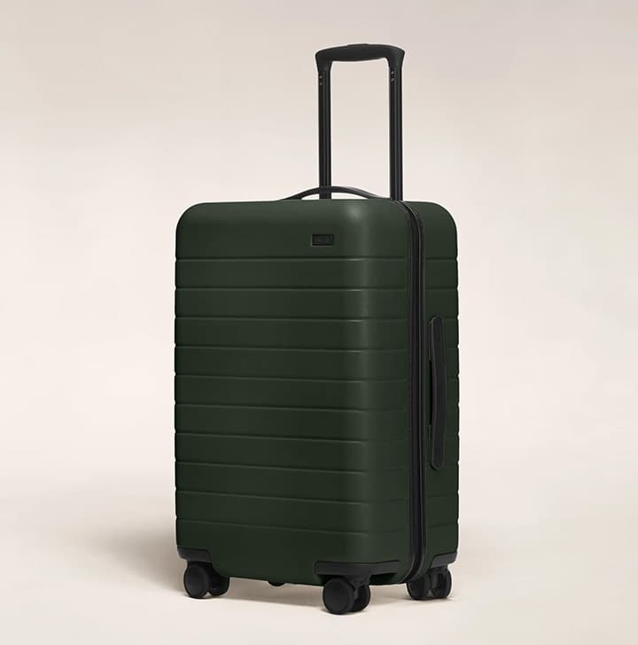 Dark green hard-shell carry-on suitcase with four spinner wheels and extended telescopic handle on a neutral background
