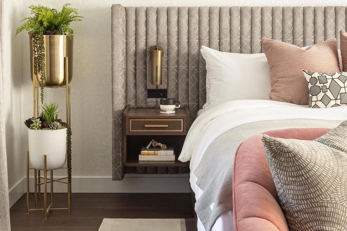 Elegant bedside vignette with upholstered bed, textured pillows, modern nightstand, and gold accent lighting in a luxury bedroom