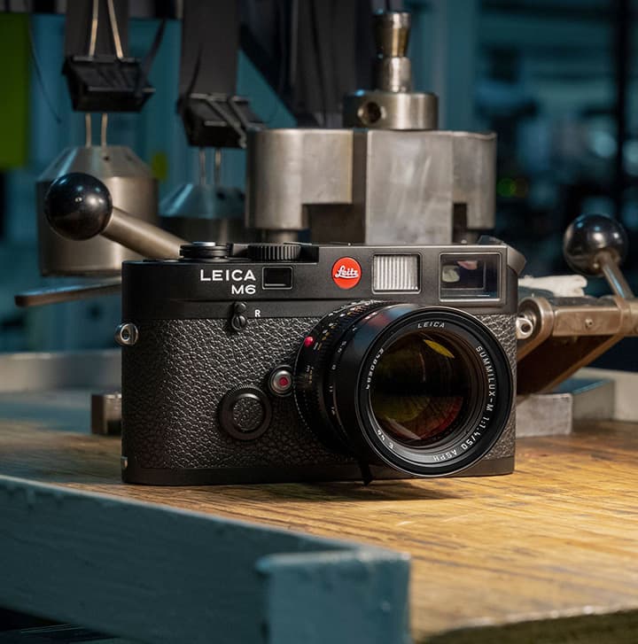 Leica M6 rangefinder film camera with lens resting on a workbench in a mechanical workshop setting