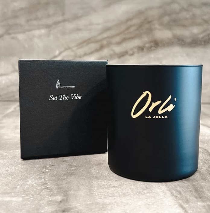 Black Orli La Jolla scented candle with gold logo displayed beside its box featuring the phrase “Set The Vibe”
