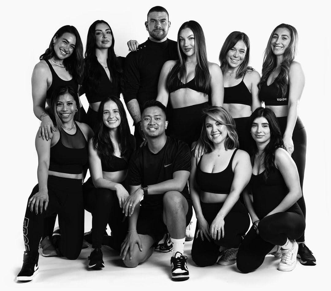 Black-and-white studio portrait of a diverse fitness training team wearing athletic apparel, posed together and smiling against a clean white background.