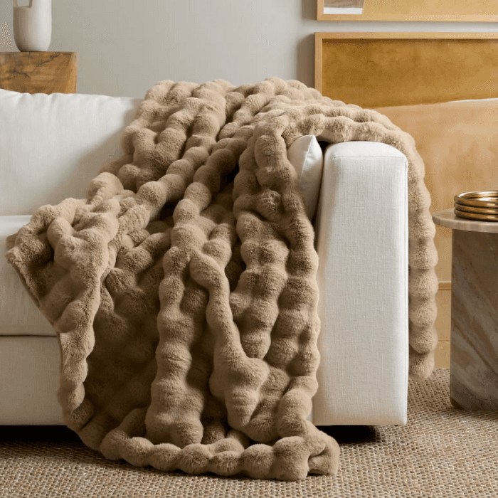Cozy chunky knit throw blanket draped over a white sofa in a warm, modern living room setting