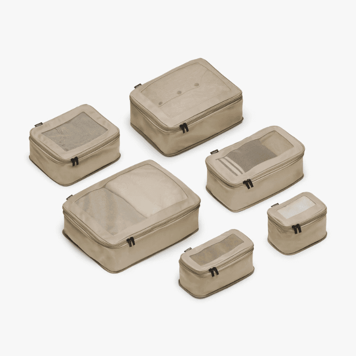 Set of beige travel packing cubes in various sizes with mesh panels, designed for organized luggage storage