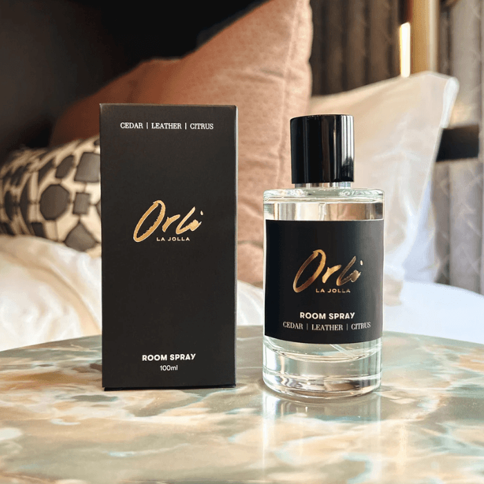 Orli La Jolla room spray bottle and packaging displayed on a bedside table in a luxury hotel-style bedroom setting