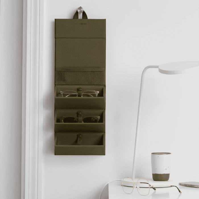 Wall-mounted fabric organizer with multiple pockets holding sunglasses and small accessories in a minimalist home interior
