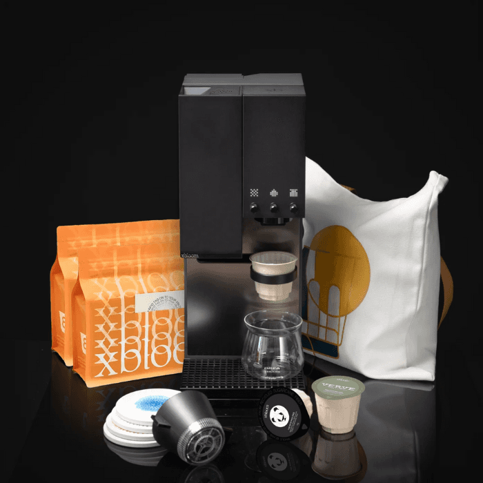 Modern espresso machine with reusable coffee pods, glass cup, and packaged coffee accessories arranged in a sleek product display