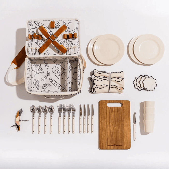 Organized picnic set with patterned insulated basket, plates, cutlery, cutting board, and accessories laid out on a white background