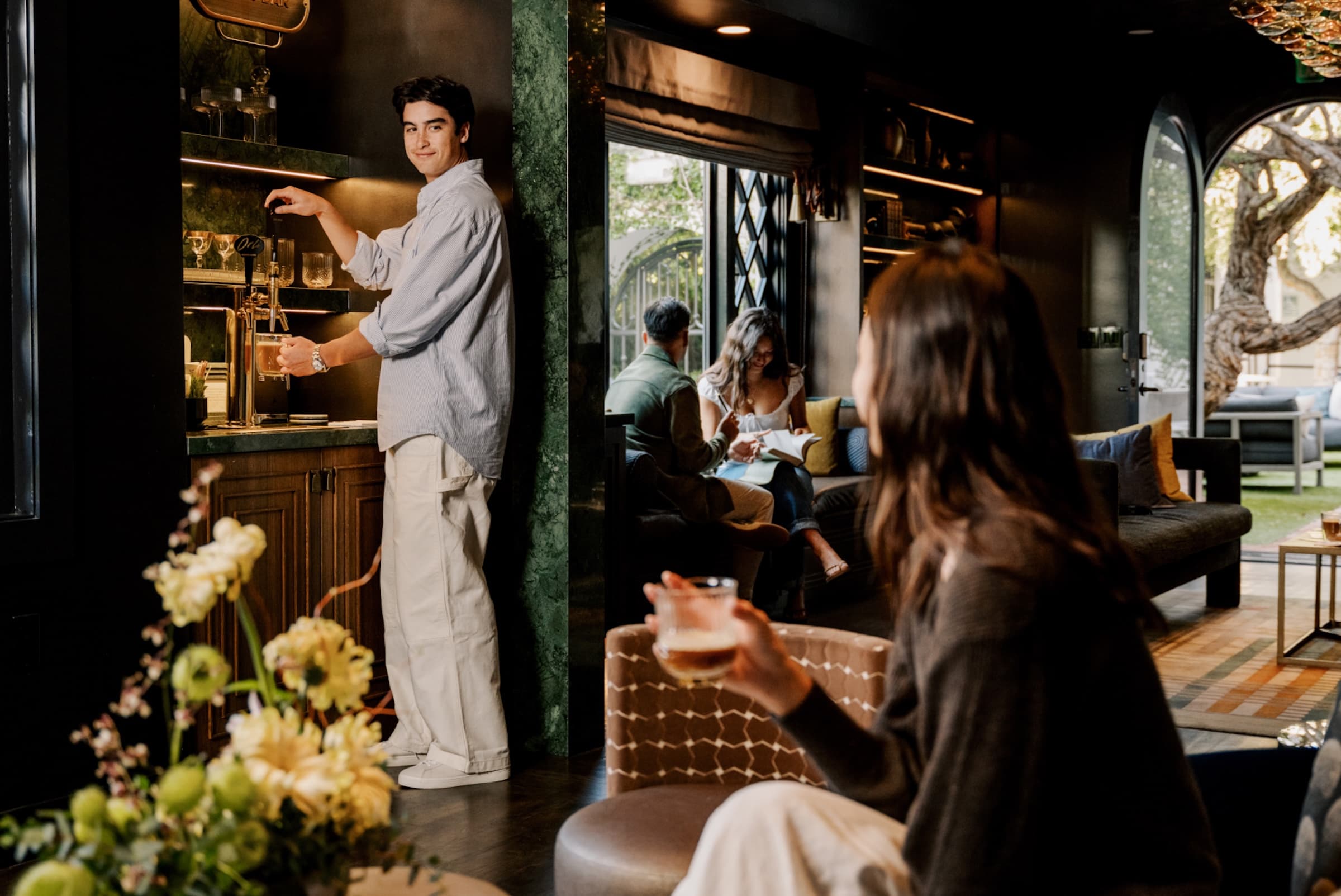 Guests enjoying cocktails inside a stylish boutique hotel lounge with warm lighting, greenery, and a relaxed social atmosphere.