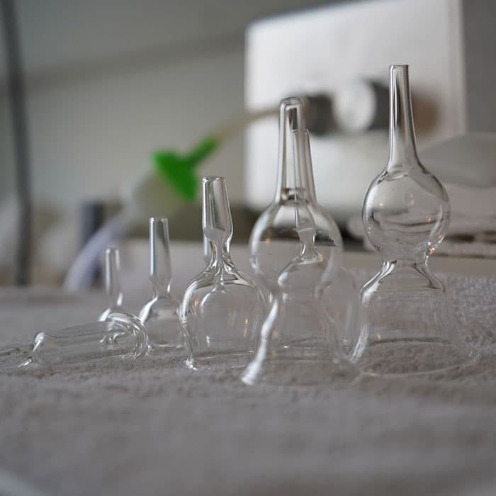 Clear glass cupping therapy cups of varying sizes arranged on a treatment table in a wellness or spa setting, with soft lighting and clinical equipment in the background.