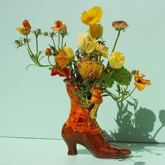 Vintage brown leather boot used as a vase holding colorful wildflowers against a soft pastel background