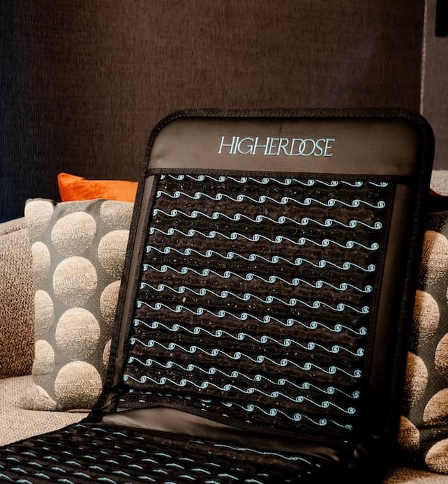 HighERDose infrared PEMF heating pad resting on a sofa, featuring a black fabric design with visible wave-pattern therapy coils for at-home pain relief and muscle recovery.