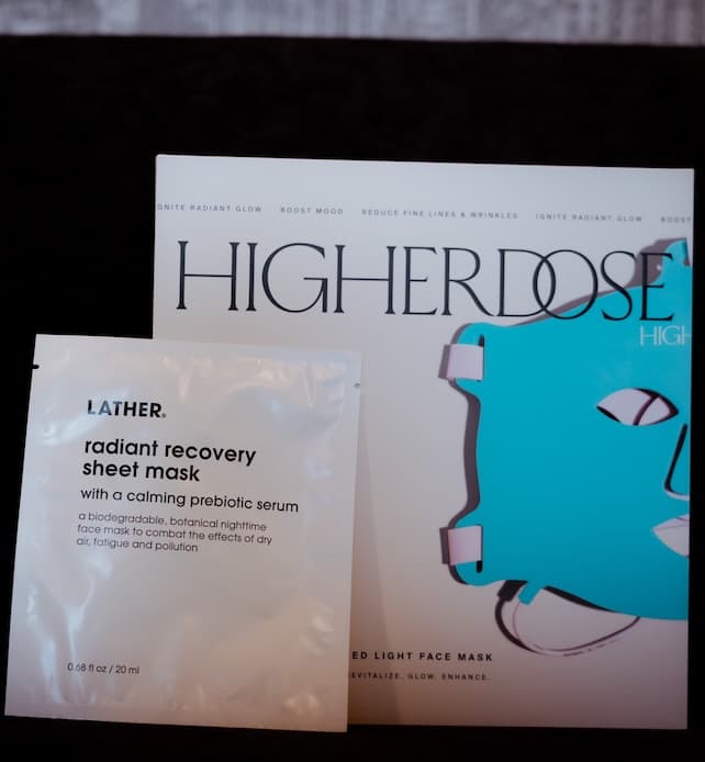 HighERDose red light face mask packaging displayed next to a LATHER radiant recovery sheet mask sachet on a dark background.
