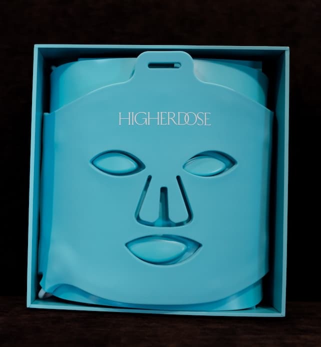 HighERDose blue LED light therapy face mask displayed in its box, featuring eye, nose, and mouth cutouts for at-home skin rejuvenation.
