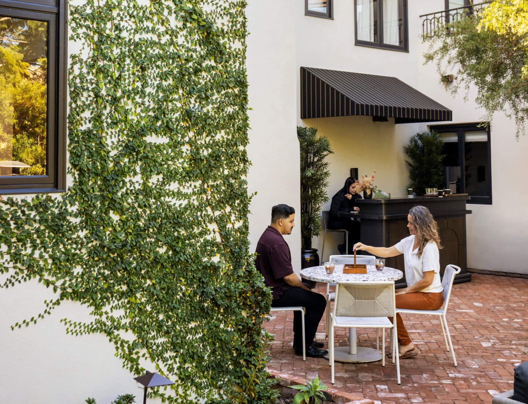 Couple dining at an outdoor café patio with brick flooring and greenery, enjoying a relaxed meal in a courtyard setting.