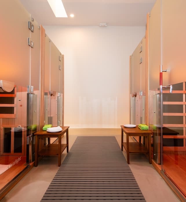 Modern spa locker room with private changing stalls, glass doors, wood benches, and neatly folded towels in a luxury wellness retreat.