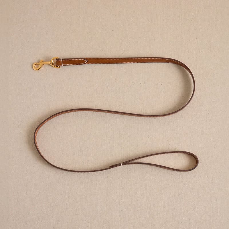 Minimalist brown leather strap with brass clasp laid flat on a neutral background, showcasing handcrafted lifestyle accessory design.