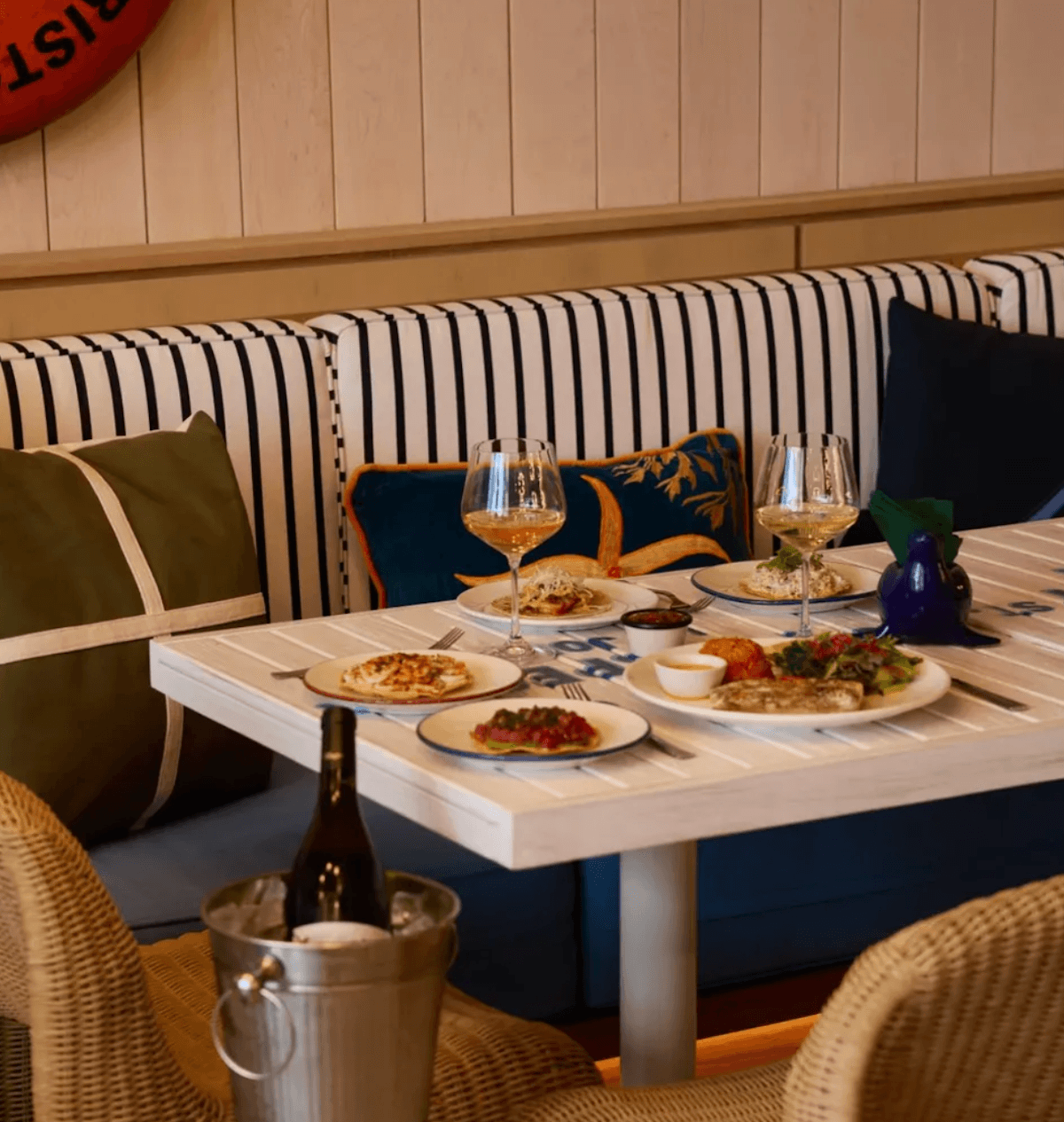 A cozy bistro table set for two, featuring shared plates and chilled white wine against striped banquette seating for an inviting, intimate dining moment.